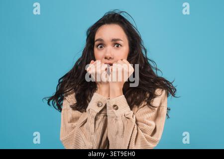 Besorgte Junge Frau Mit Langen Dunklen Haaren, Die Angst Und Stress Zeigen, Blauer Hintergrund Stockfoto