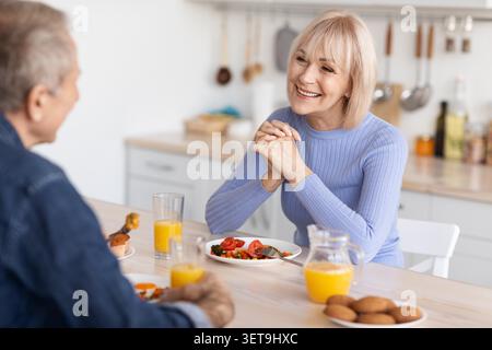 Fröhliches Älteres Kaukasisches Paar Genießt Das Gemeinsame Frühstück Zu Hause, Lächelt Und Redet Stockfoto