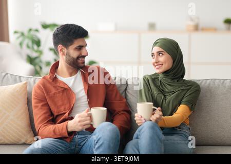 Lächelnder Junger Mann Und Frau, Die Cups Auf Der Couch Zu Hause Halten, Lifestyle-Konzept Stockfoto