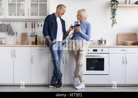 Glückliches Älteres Kaukasisches Paar Genießt Wein Und Lächeln In Moderner Küche, Home Lifestyle Stockfoto