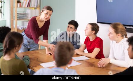 Eine Lehrerin spricht mit aufmerksamen Schülern im Teenageralter, die am Tisch sitzen Stockfoto