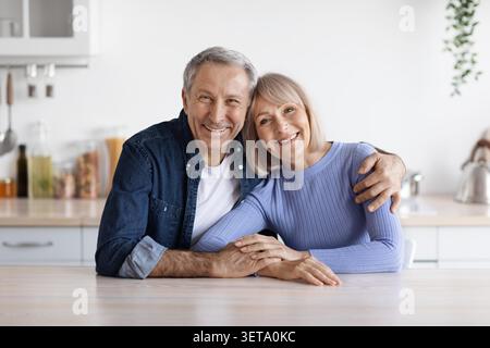 Glückliches Älteres Kaukasisches Paar, Das Sich Zu Hause, In Der Küche, Umschließt Und Lächelt Stockfoto