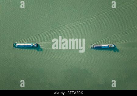 Von oben nach unten sehen Sie zwei Binnenschiffe, die unter ruhigen Bedingungen einen Fluss inmitten üppig grüner Gewässer befahren. Stockfoto