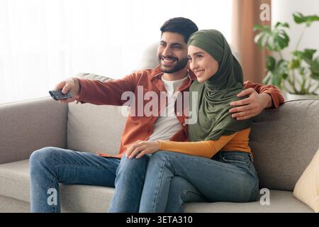Glückliches Junges Muslimisches Paar, Das Zu Hause Zusammen Fernsehen Sieht, Gemütlicher Entspannter Abend Stockfoto