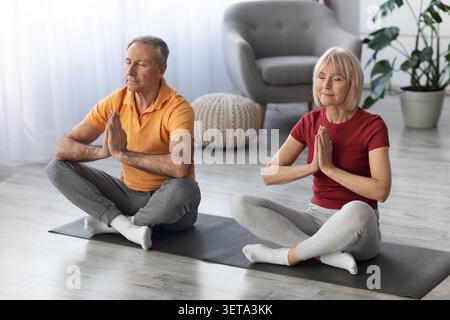 Älteres Kaukasisches Paar Praktiziert Gemeinsam Meditation Zu Hause, Entspannter Zustand, Wellness-Konzept Stockfoto