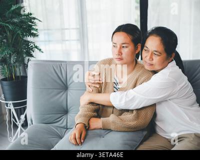 Asiatische Betreuerin umarmt eine junge Frau in einem gemütlichen Wohnzimmer, zeigt Unterstützung der Familie, Empathie, emotionale Heilung, Komfort, Sicherheit, Vertrauen, Bon Stockfoto