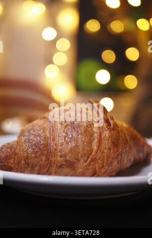 Frisch gebackenes Croissant auf einem weißen Teller mit verschwommenem Licht Stockfoto