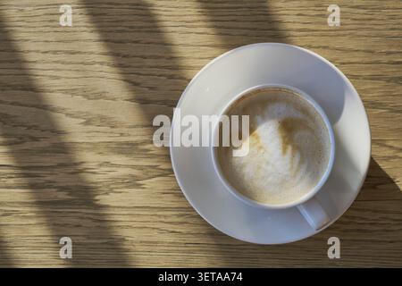 Kaffeetasse mit Latte Art Schaum auf einem Holztisch mit Sonnenschirm Stockfoto