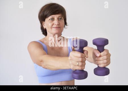 Kaukasische reife Frau, die mit Kurzhanteln in blauer Sportbekleidung arbeitet Stockfoto