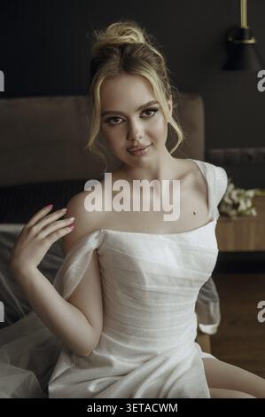 Schöne Braut Mode Porträt in Hochzeit Luxus Kleid mit Spitze und Kristallen in dunklem Innenraum Blonde glückliche Frau trägt Hochzeit weißes Kleid mit Wed Stockfoto