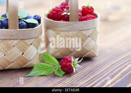 Heidelbeeren und Himbeeren in kleinen Birkenrindenkörben auf hölzernem Hintergrund. Ernte von Waldbeeren, Vitaminen und gesundheitlichen Vorteilen Stockfoto
