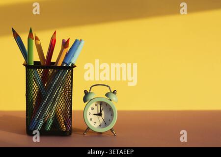 Arbeitsbereich mit Wecker und Bürobedarf auf gelbem Hintergrund. Zurück zur Schule. Schulwerkzeuge, Kopierraum Stockfoto