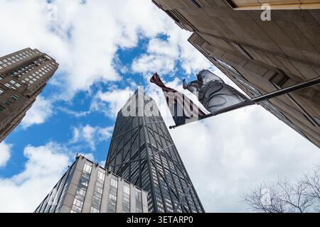 Chicago, USA - 15. April 2025: Die Wolkenkratzer von Chicago erheben sich in einen blauen Himmel, in der Nähe winkelt eine amerikanische Flagge Stockfoto