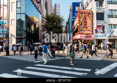 Tokio, Japan - 4. August 2024: Eine lebhafte Straßenszene in Shinjuku, Tokio, fängt Fußgänger ein, die einen Zebraübergang überqueren. Das Bild zeigt einen Bustli Stockfoto
