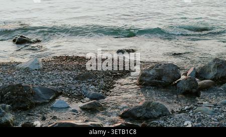 Felsige Küste mit Meereswellen, die auf große Kieselsteine und Steine aus nächster Nähe Rollen. Stockfoto