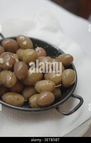 Marinierte grüne und lila Oliven in kleiner ovaler Metallpfanne serviert als Vorspeise auf einer Serviette mit weißem Tuch, Restaurant in der Nähe Stockfoto