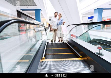 Paare, die einen Tag in der Mall verbringen, während sie den Escalator in einem modernen Einkaufszentrum nutzen Stockfoto