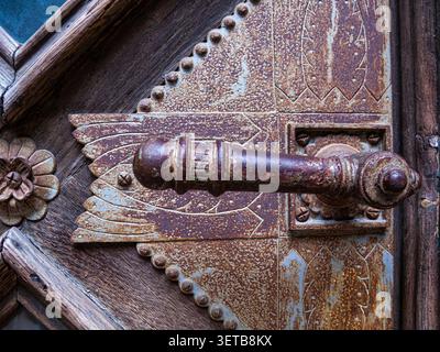 Ein rostiger Türgriff ist an einer Holztür in Tschernowitz, Ukraine, mit detaillierten Designs und verwitterten Texturen zu sehen, die das Alter anzeigen. Stockfoto