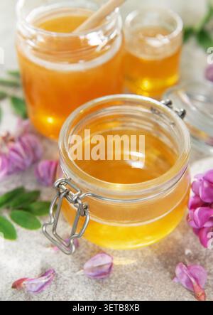 Frischer biologischer Akazienhonig in einem Glas mit Blüten auf Steingrund Stockfoto