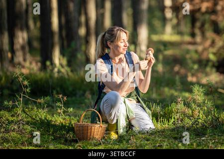Eine lächelnde Pilzjägerin fand frische essbare Pilze im herbstlichen Kiefernwald. Stockfoto
