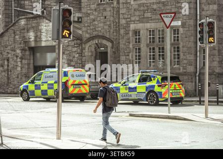 Garda Polizei patrouilliert Autos, die vor dem historischen Steingebäude Pearse Street Garda Station im Stadtzentrum von Dublin geparkt sind, mit einem Mann, der die Straße überquert. Stockfoto
