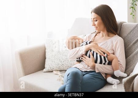 Mutter verbindet sich mit dem Baby während des Stillens, während sie sich im gemütlichen Wohnzimmer entspannt Stockfoto