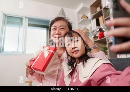 Asiatische Großmutter und Enkelin machen Selfie mit Smartphone, während sie die Geschenkbox zu Hause zur Geburtstagsfeier halten Stockfoto