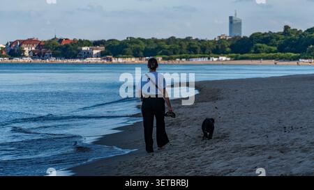Frau wandert Hund am Ostseestrand am sonnigen Sommertag Stockfoto