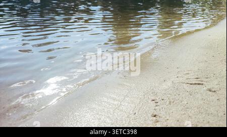 Ein Blick aus der Luft oder von oben auf ein ruhiges Seeufer, wo das Wasser ruhig ist und Himmel und Wolken perfekt reflektiert. Flaches Wasser trifft auf feinen Sand Stockfoto