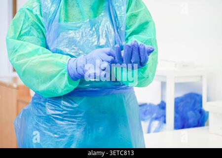 Das medizinische Fachpersonal trägt persönliche Einweg-Schutzausrüstung in einer klinischen Umgebung, um eine sorgfältige Vorbereitung auf chirurgische oder chirurgische Eingriffe zu demonstrieren Stockfoto