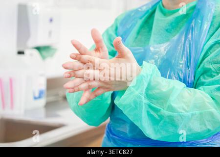 Ein medizinisches Fachpersonal in einem grünen Schutzmantel übt eine gründliche Handhygiene mit antiseptischem Gel aus, um eine sterile Atmosphäre und ensu zu erhalten Stockfoto