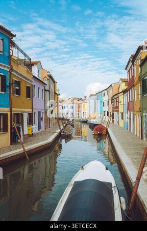 Burano Island, Venedig, Italien, ein schmaler Kanal gesäumt von lebhaften, farbenfrohen Häusern und kleinen Booten unter blauem Himmel. Stockfoto