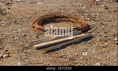 Auf der kiesigen Oberfläche einer Außenbaustelle befindet sich neben mehreren spitzen Holzpfählen ein Bündel aus rostigem Stahldraht Stockfoto