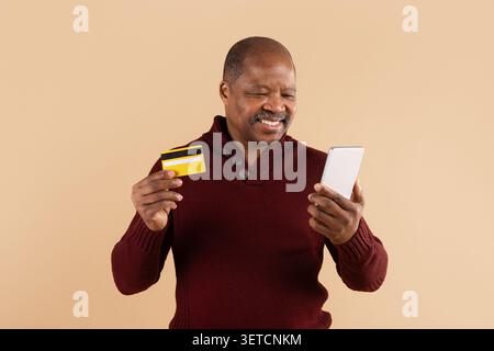Reifer Afroamerikaner lächelt, während er Smartphone und Kreditkarte hält Stockfoto