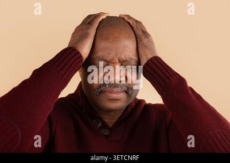 Reifer schwarzer Mann mit Händen auf dem Kopf, Kopfschmerzen, Augen geschlossen Stockfoto