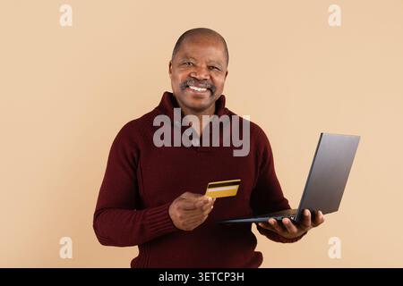 Reifer Afroamerikaner lächelt, während er Laptop und Kreditkarte hält Stockfoto