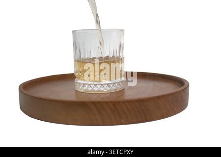 Nahaufnahme des Bieres, das aus der Flasche in das Glas gegossen wird. Blick auf das prickelnde Bier in einem Glas auf einem Holztablett. Stockfoto