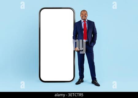Reifer schwarzer Geschäftsmann im Anzug mit Mappe, der neben einem riesigen leeren Smartphone steht Stockfoto
