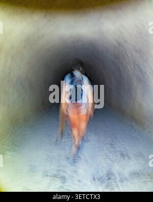 Person, die durch einen dunklen Tunnel in Richtung eines fernen Lichtes mit Bewegungsunschärfe geht Stockfoto