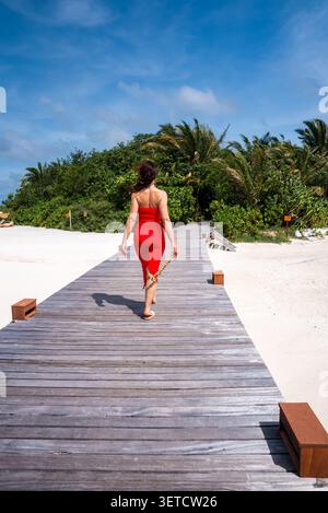 Frau geht barfuß auf der Promenade zum Malediven Beach Retreat Stockfoto