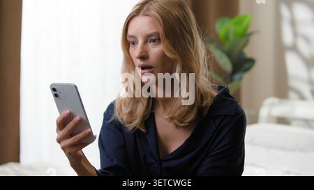 Gadget süchtig schockiert erstaunte weiße Frau Benutzer mit Handy schauen schockierende Video-Inhalte weibliches Mädchen mit Smartphone erstaunlich mit schlecht Stockfoto