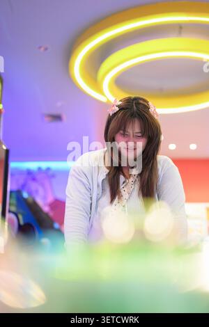 Ein vertikales Lifestyle-Porträt eines fokussierten südostasiatischen Thai-Isan-Teenagers, das beim Spielen einer Spielkonsole nach unten blickt. Aufgenommen aus einer Lo Stockfoto