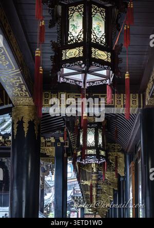 Chongqing, China - 11. Juni 2026 - eine verzierte, sechseckige chinesische Laterne hängt anmutig von der dunklen Holzdecke eines überdachten Gehwegs. Es ist kompliziert Stockfoto