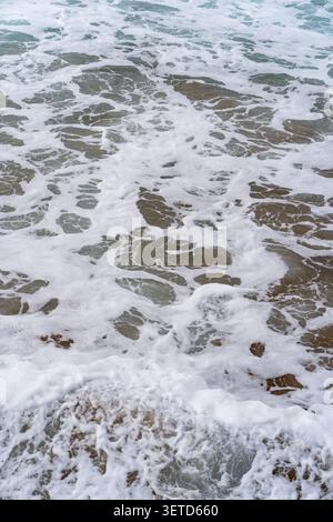 Nahaufnahme sanfter Ozeanwellen mit weißen Schaummustern, die über den Sandboden fließen Stockfoto