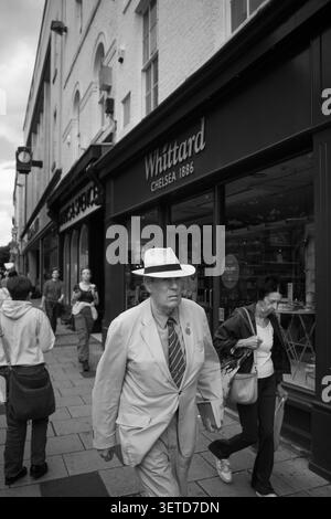 Ein älterer Mann in weißem Anzug und Fedora läuft entlang einer geschäftigen Einkaufsstraße in York, Großbritannien. Stockfoto