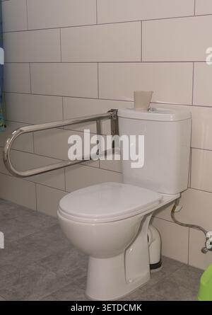 Ein sauberes, minimalistisches Badezimmer mit einer weißen Keramik-Toilette und einem Sicherheitsgriff aus Metall für die Pflege älterer Menschen Stockfoto
