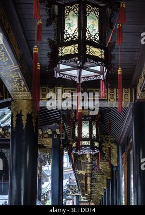 Chongqing, China - 11. Juni 2026 - eine verzierte, sechseckige chinesische Laterne hängt anmutig von der dunklen Holzdecke eines überdachten Gehwegs. Es ist kompliziert Stockfoto
