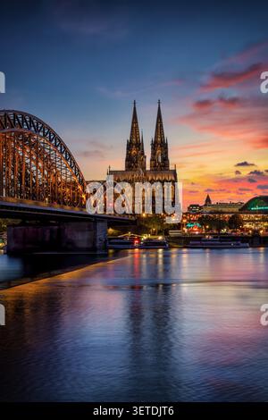 Der beleuchtete Kölner Dom mit der Hohenzollernbrücke und dem Rhein in der Sommerdämmerung Stockfoto