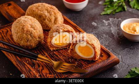 Traditionelle schottische Eier auf einem Holzbrett, auf dunklem Hintergrund. Stockfoto