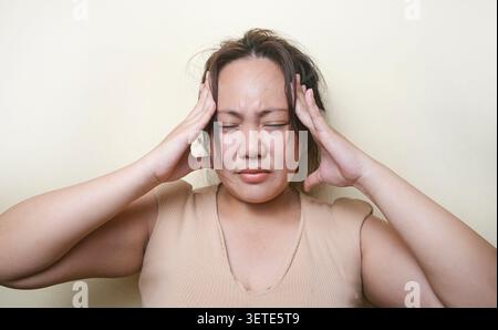 Junge Frau, die an Kopfschmerzen leidet, während sie ihre Schläfe mit geschlossenen Augen hält. Stockfoto
